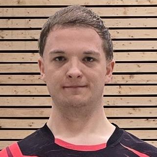 Ein Badmintonspieler in rotem Trikot steht auf einem Court, im Hintergrund ist das Netz und einige Federbälle verteilt.