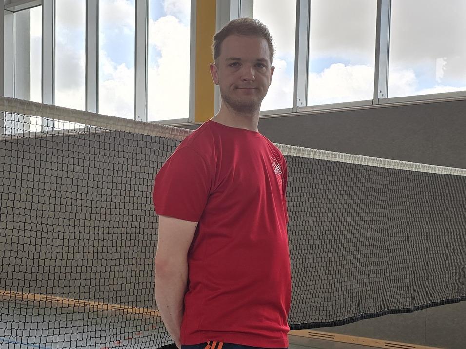 Ein Mann steht vor einem Badmintonnetz in einer Halle, bereit für ein Spiel auf dem Indoorplatz.