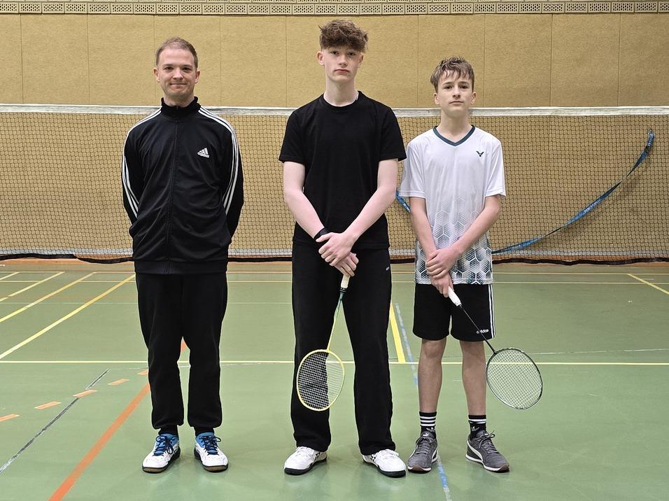 Drei junge Männer posieren vor einem Badmintonfeld, bereit für das Spiel.