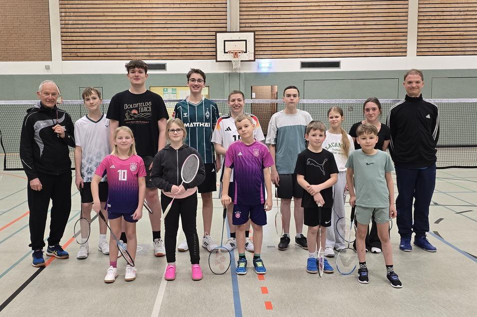 Kinder und Jugendliche Badmintonspieler:innen mit ihren Trainern vor einem Netz in der Sporthalle.