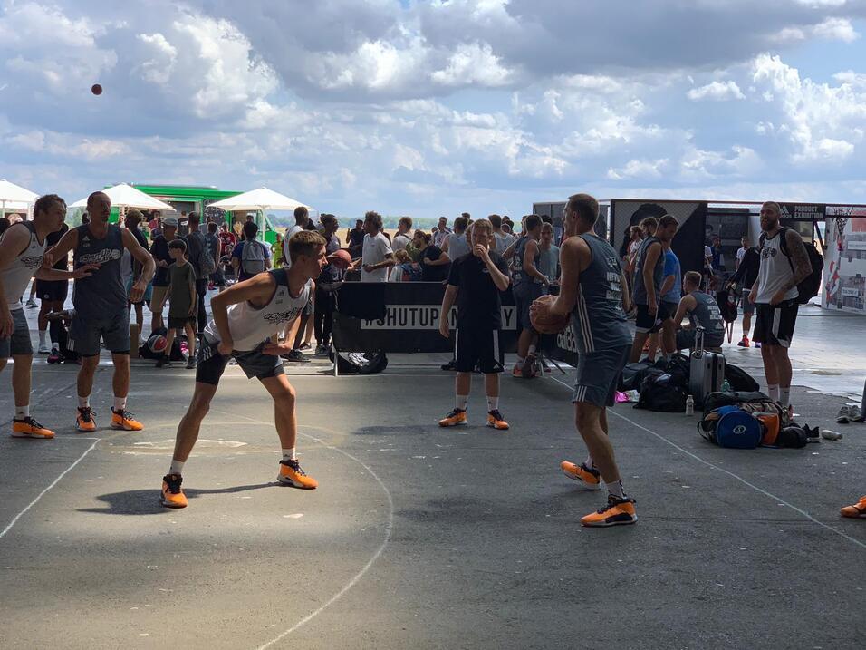 Zwei Gruppen von Basketballspielern üben in einer Bewegung, umgeben von Zuschauern auf einem Freiluftplatz.