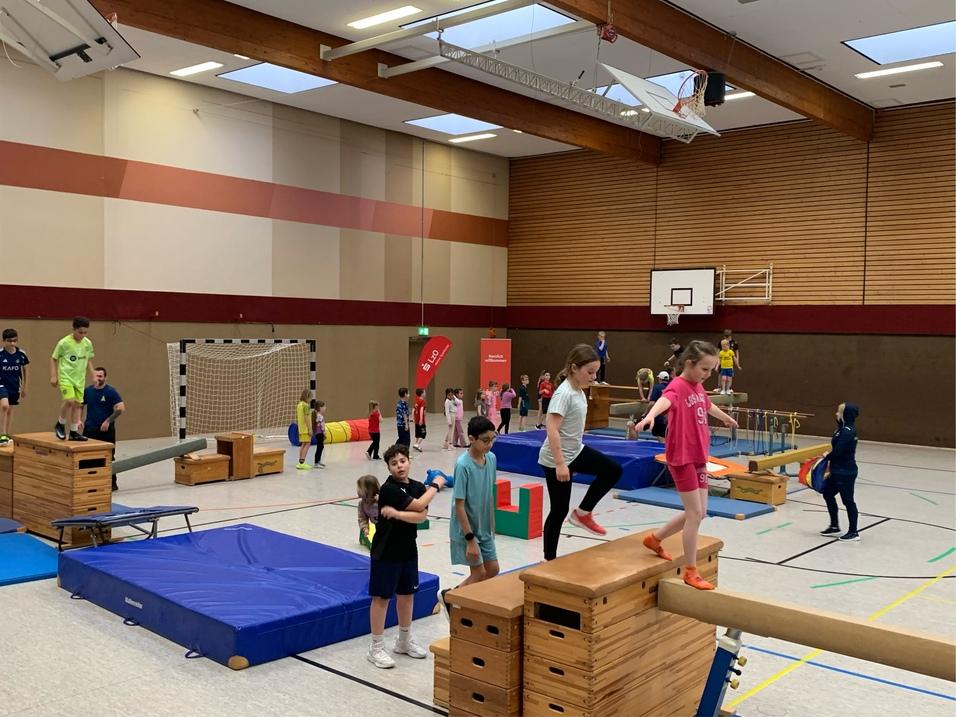 Kinder haben Spaß auf dem Gymnastikboden mit verschiedenen Turngeräten.