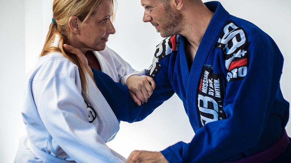 Zwei Kampfsportler in BJJ-Anzügen üben eine Techniken mit Körpersprache im Gesichtsausdruck sichtbar.