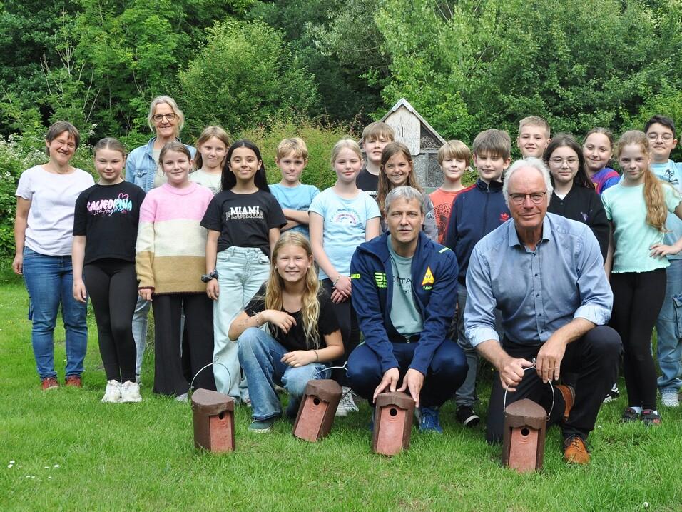 Gruppe von Kindern und Erwachsenen, posierend auf einer Wiese mit Nistkästen im Vordergrund.
