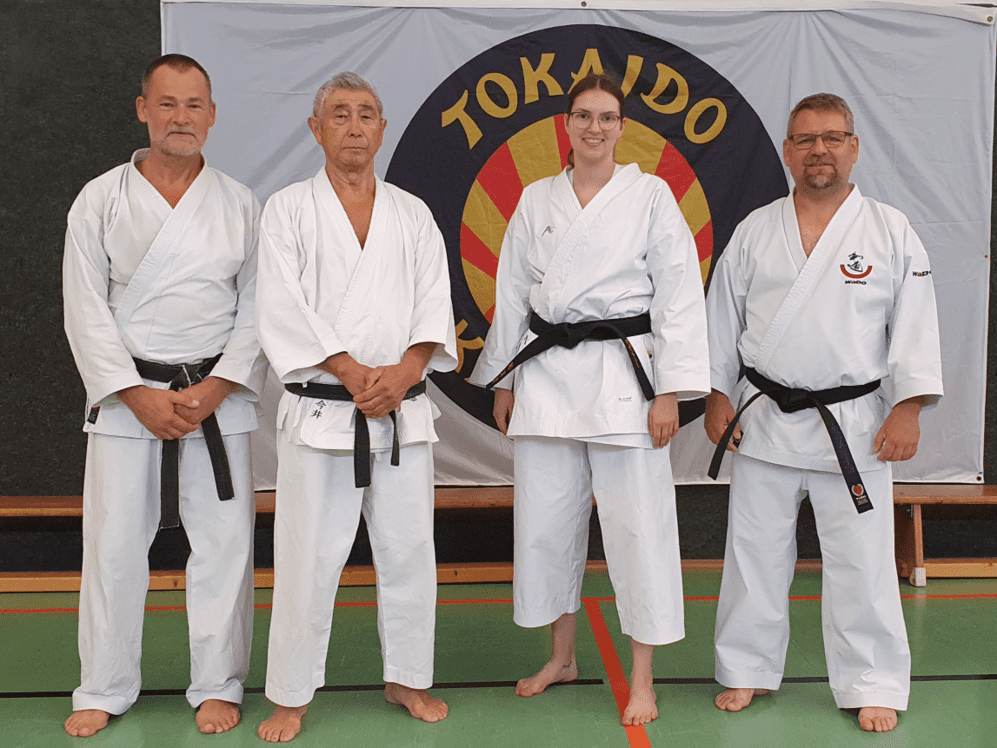 Vier Karateka in traditioneller Kleidung stehen zusammen und lächeln für ein Gruppenfoto.