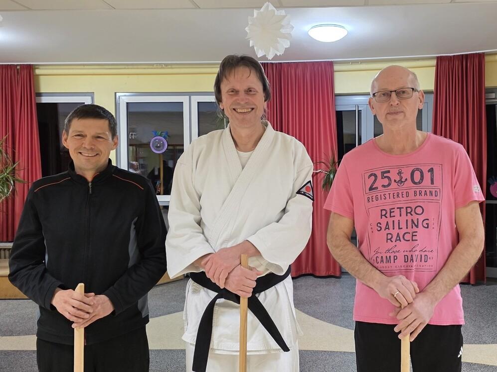 Drei Männer in Karateanzügen posieren lächelnd für ein Foto.