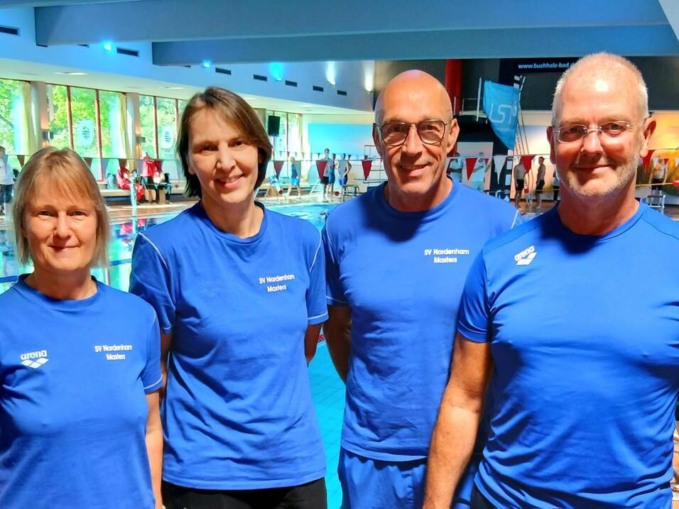 Vier Schwimmer in blauen T-Shirts des SV Nordenham Masters stehen lächelnd am Beckenrand eines Schwimmbads.