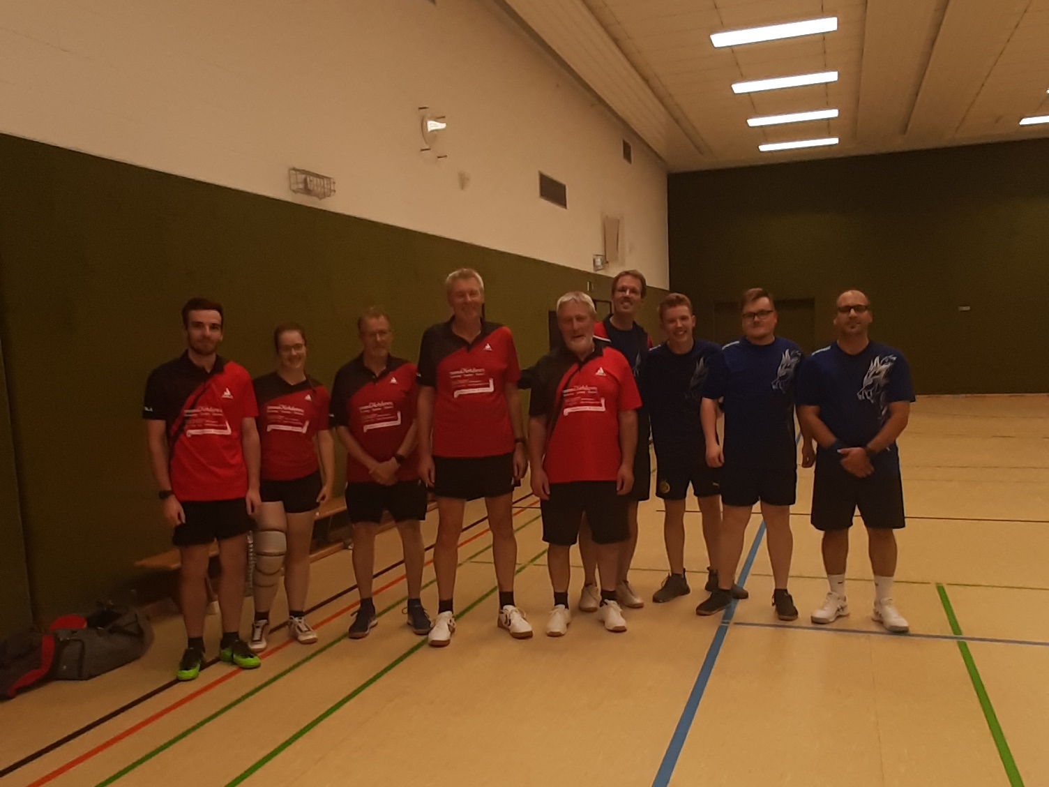 Gruppe von Sportlern in roten und blauen Trikots stehen auf einem Sportplatz in einer Turnhalle.