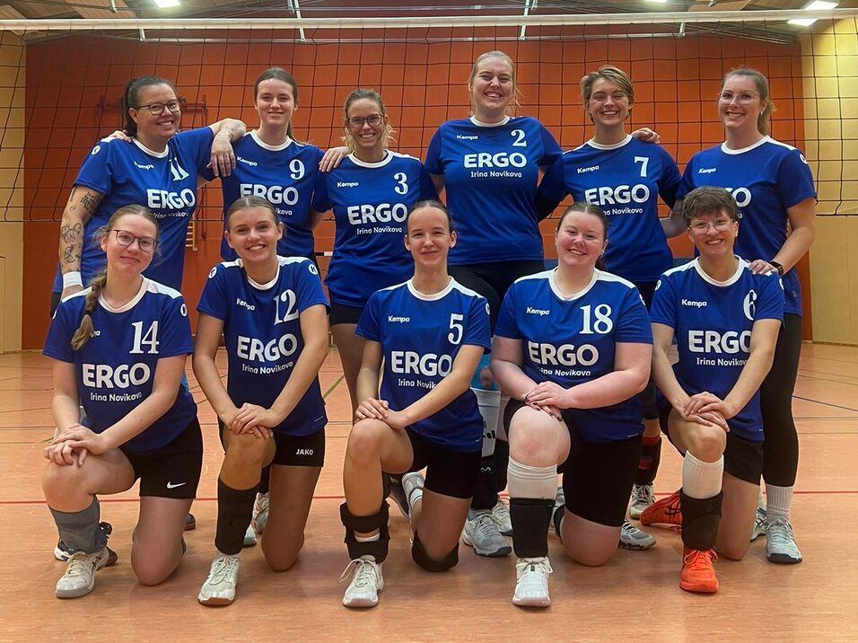 Teamfoto einer Volleyballmannschaft, Spielerinnen in einheitlichen Trikots, lächeln in die Kamera auf dem Spielfeld