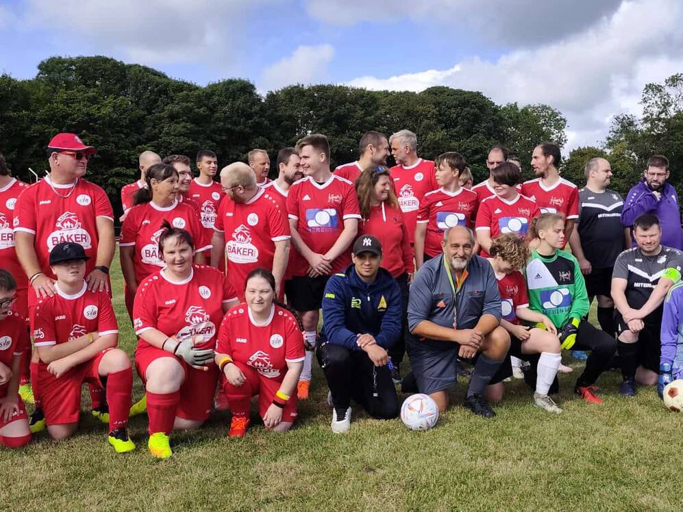 Gruppe von Fußballspielern in roten und dunklen Trikots steht und kniet auf einem Rasenplatz.