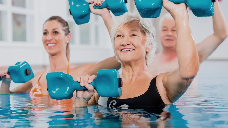 Gruppe von drei Personen im Wasser mit blauen Hanteln, lächelnd und aktiv bei einem Wasserfitnesskurs.