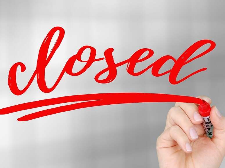 Hand, die mit einem roten Marker das Wort „closed“ auf einen unscharfen Hintergrund schreibt.