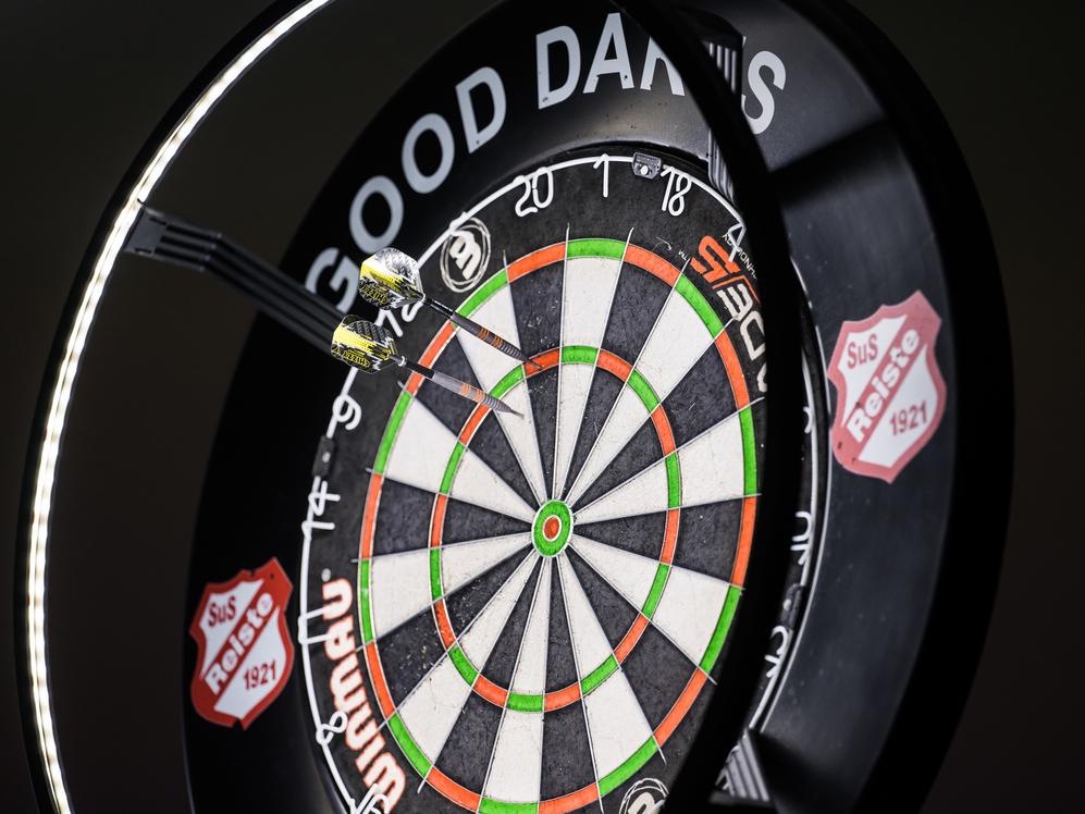 Zwei Pfeile stecken in einem Dartboard, umringt von einem beleuchteten Rahmen mit der Aufschrift „GOOD DARTS“.